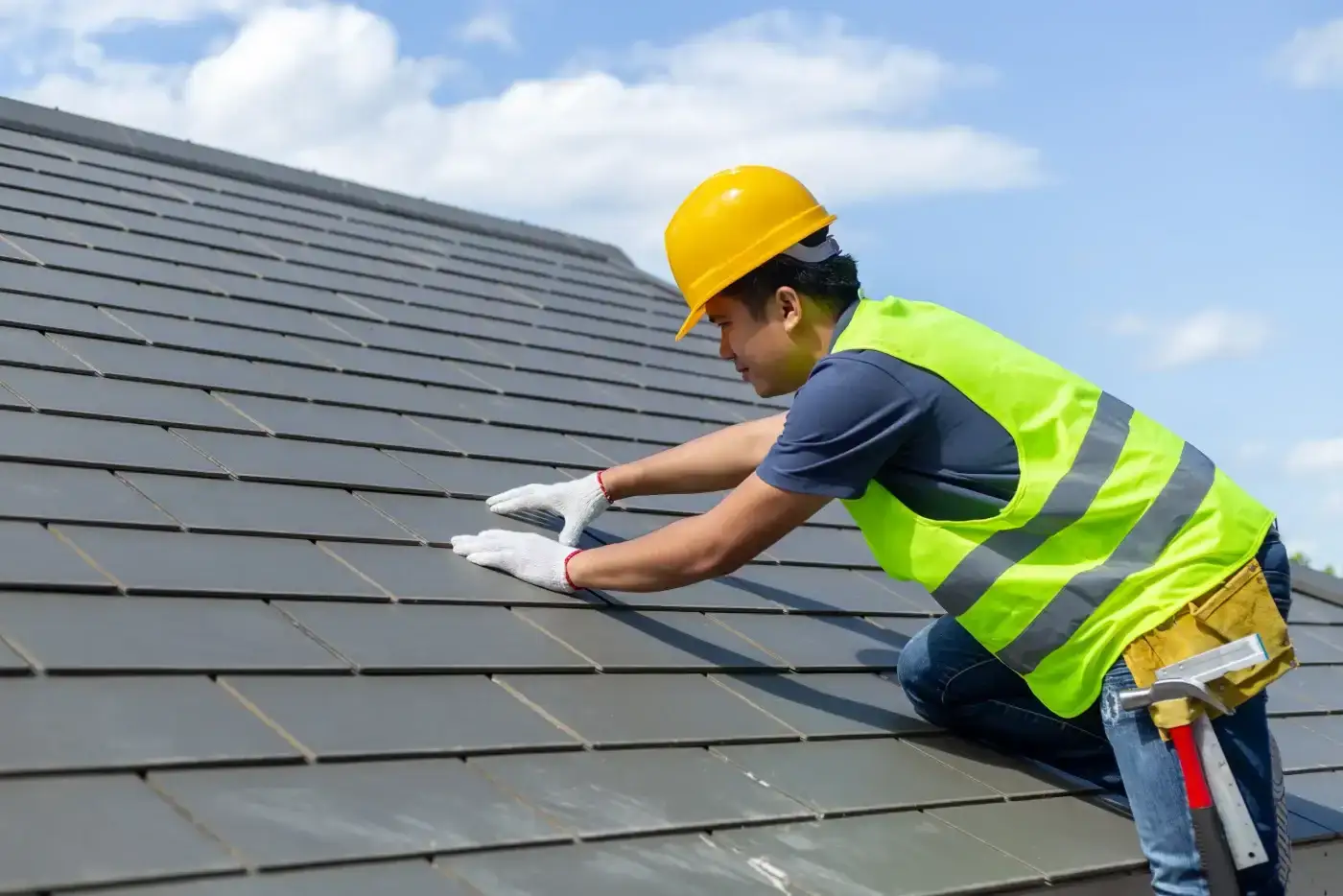 A roofer in a yellow hard hat carefully aligns synthetic roofing tiles on a residential roof pitch.